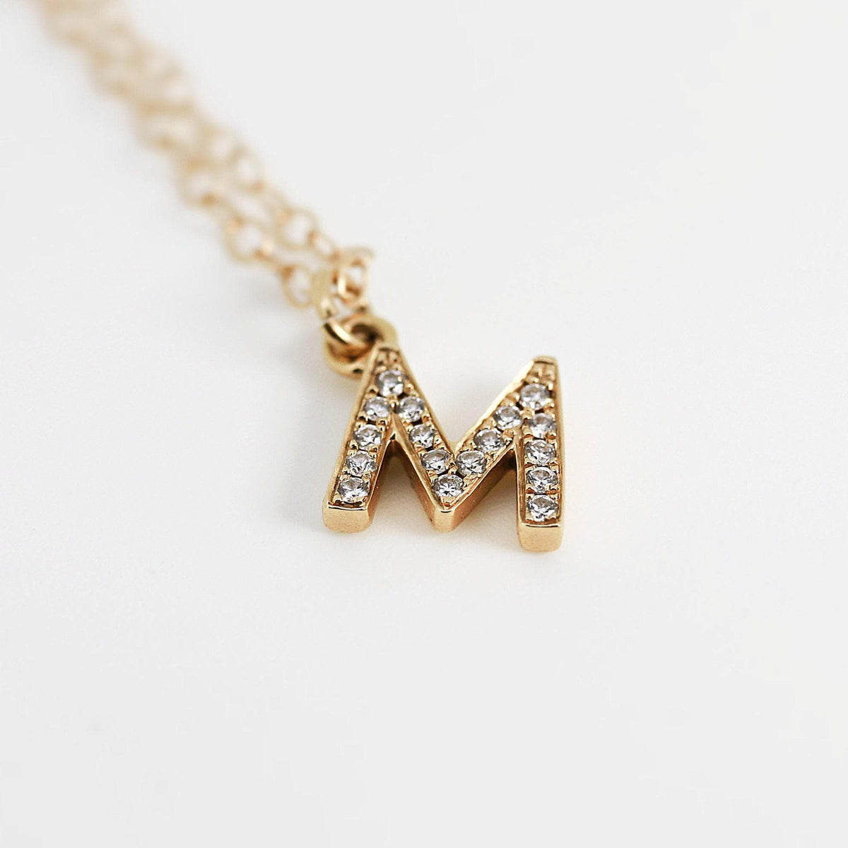 A gold letter M charm pavé set with tiny diamonds attached to the end of a delicate gold chain.