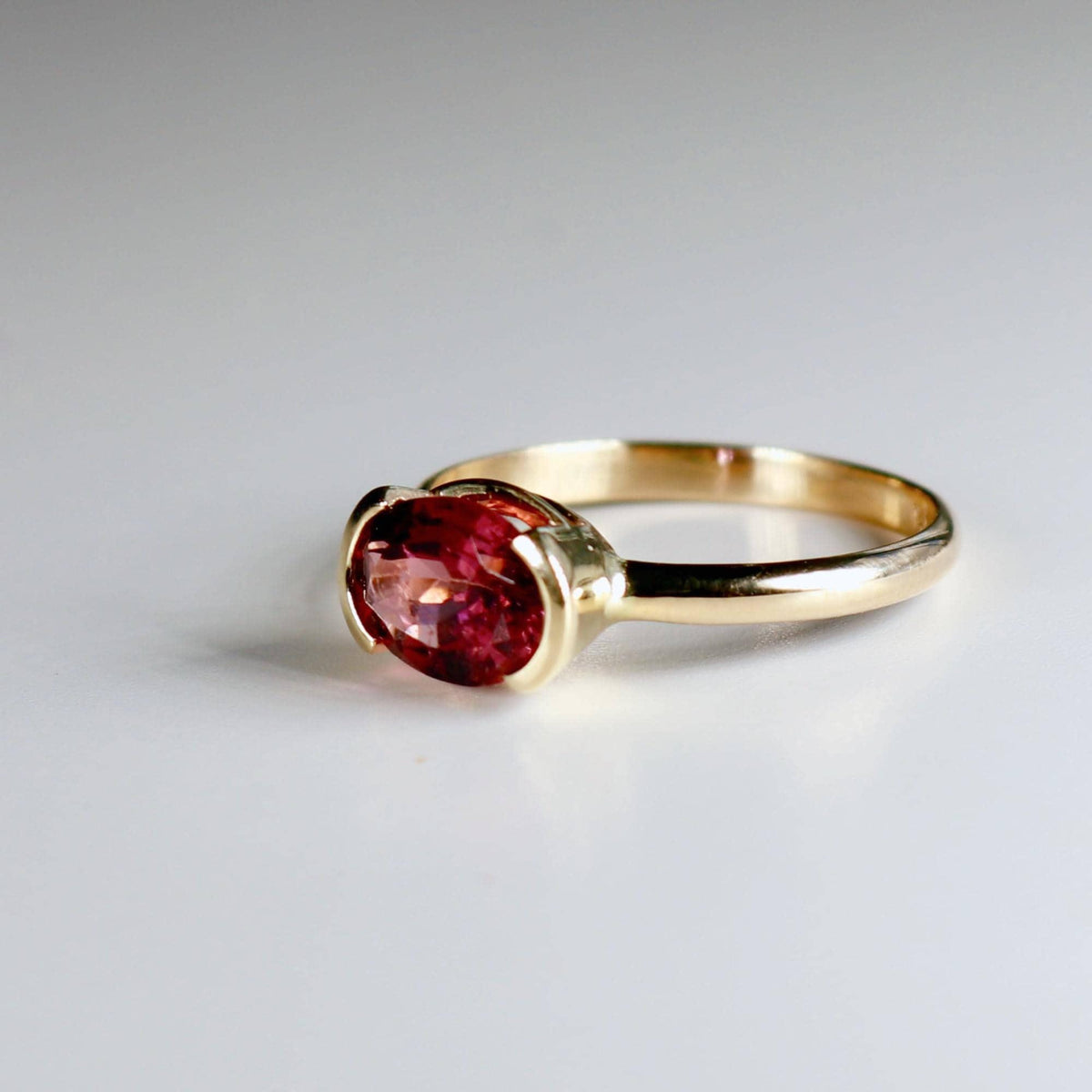An angled view of the gold ring showcasing the faceted pink tourmaline stone secured horizontally in a bezel setting.