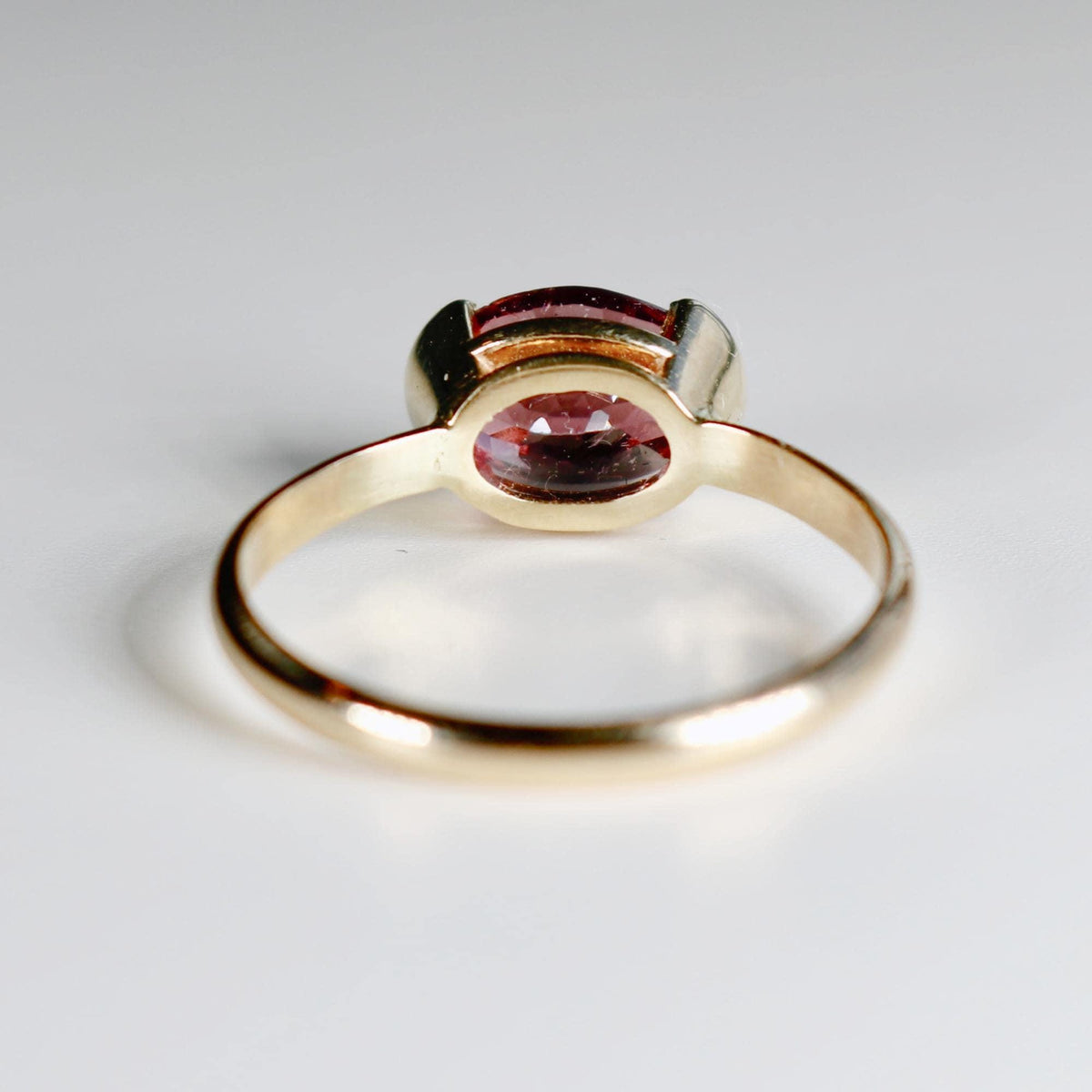 A rear-facing profile view of the gold ring resting on a white surface, showing the gallery and underside of the pink tourmaline setting.
