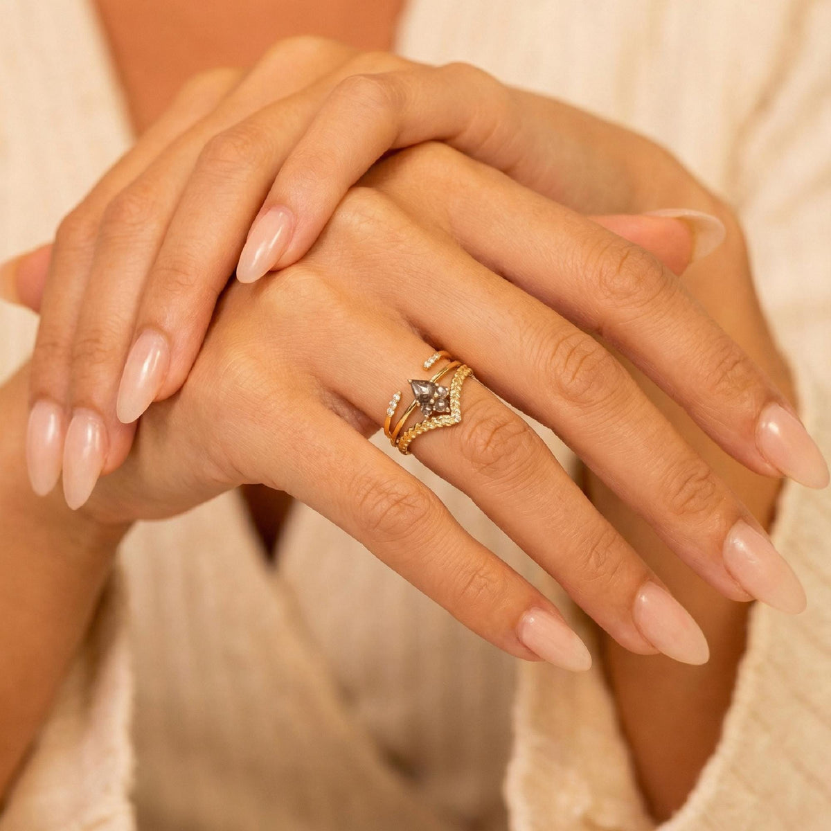 A person wearing a gold ring stack with a central kite-shaped salt and pepper diamond on their ring finger.