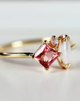 Close-up side view of a gold ring featuring a prong-set square pink tourmaline and a marquise-cut opal against a light background.