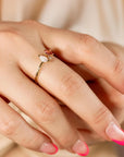 A gold ring featuring a pink stone and an opal worn on a hand with French manicure nails, against a silky fabric background.