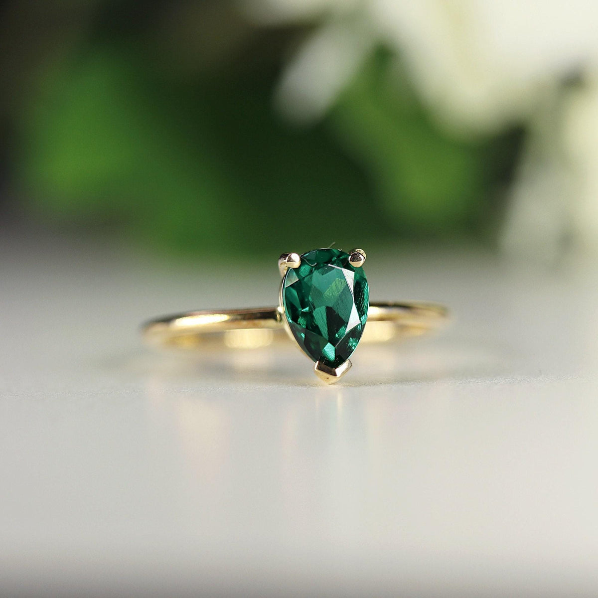 Close-up profile of the gold pear-shaped green gemstone ring against a blurred background.
