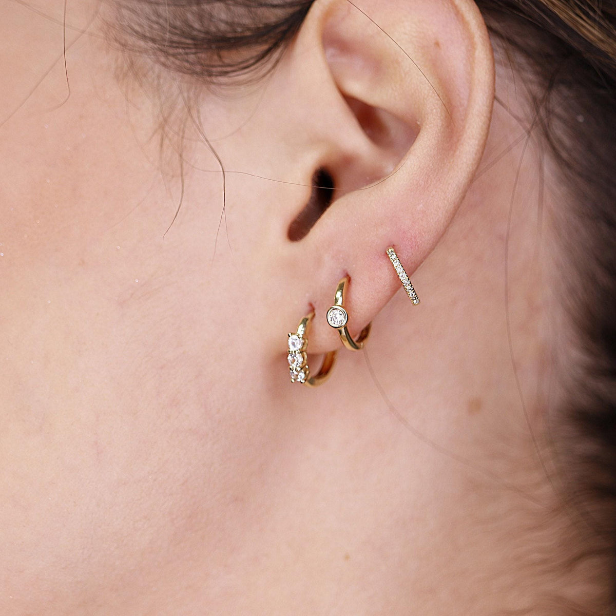 Close-up of a curated ear stack featuring three gold hoop earrings and a delicate pavé helix ring.