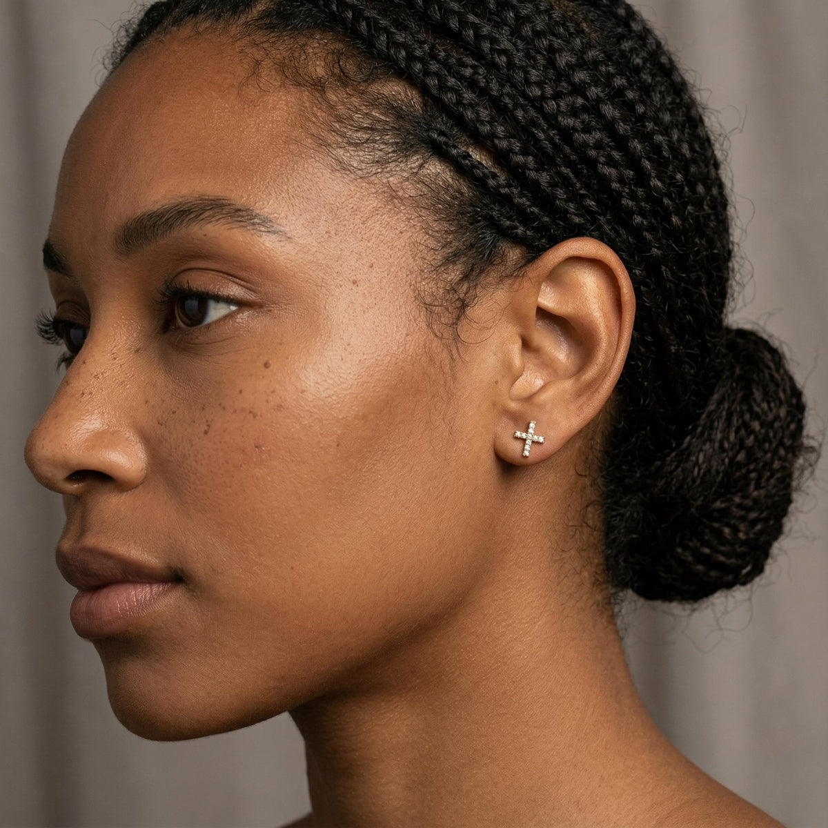 A close-up profile view of a person wearing a small X-shaped diamond stud earring on their earlobe.