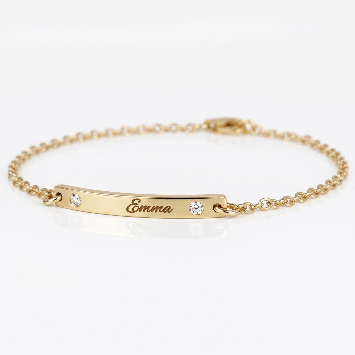 A delicate gold chain bracelet featuring a curved engraved nameplate bar with the name Emma and two small inset diamonds.