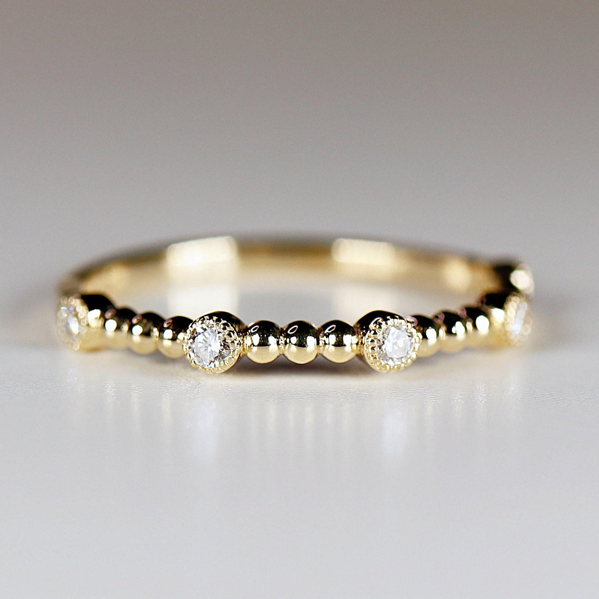 Front view of a thin gold ring featuring evenly spaced round bezel-set diamonds and textured gold bead accents.