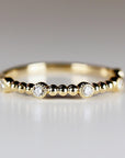 Front view of a thin gold ring featuring evenly spaced round bezel-set diamonds and textured gold bead accents.