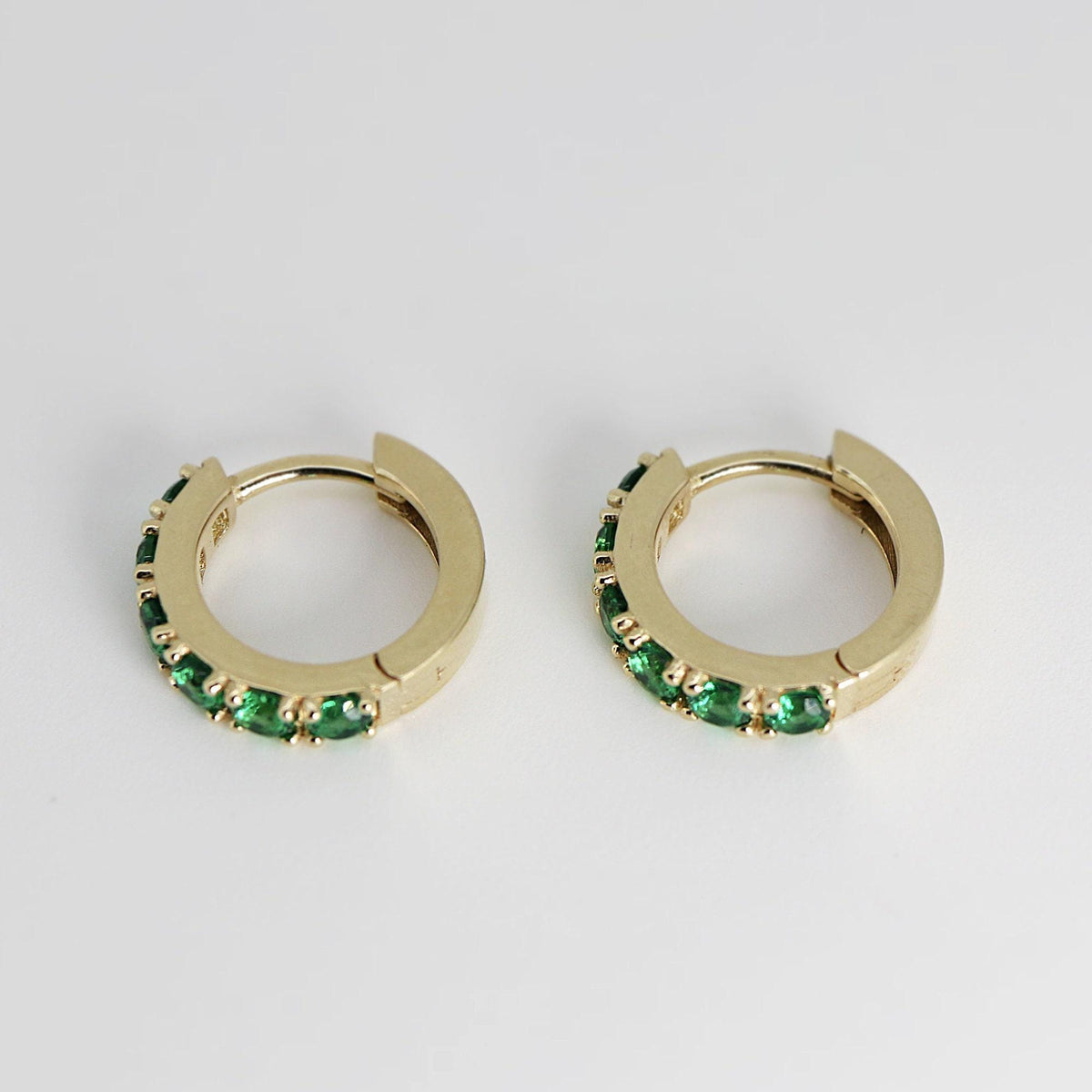 Top-down view of two gold hoop earrings displaying the inner clasp mechanism and green gemstone channel setting.