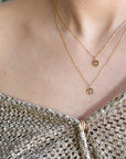 A close-up view of a person wearing an off-the-shoulder gold knit top and two layered gold chain necklaces with small circular pendants.