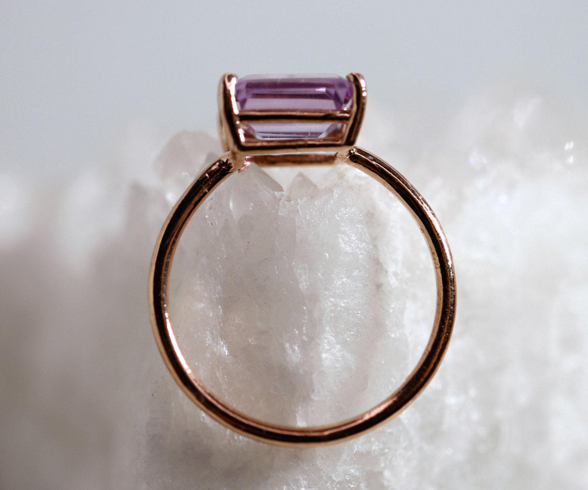 A front-facing view of the circular gold band and rectangular purple gemstone, displayed upright on a white crystal cluster.