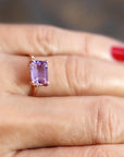 A close-up shot of a hand with red manicure wearing the thin gold ring with a vertically oriented rectangular purple gemstone.