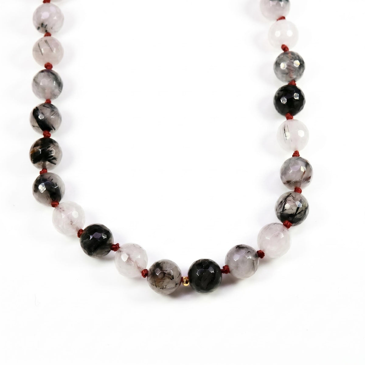 Close-up of faceted black rutilated quartz beads strung on red silk with knots between each bead.