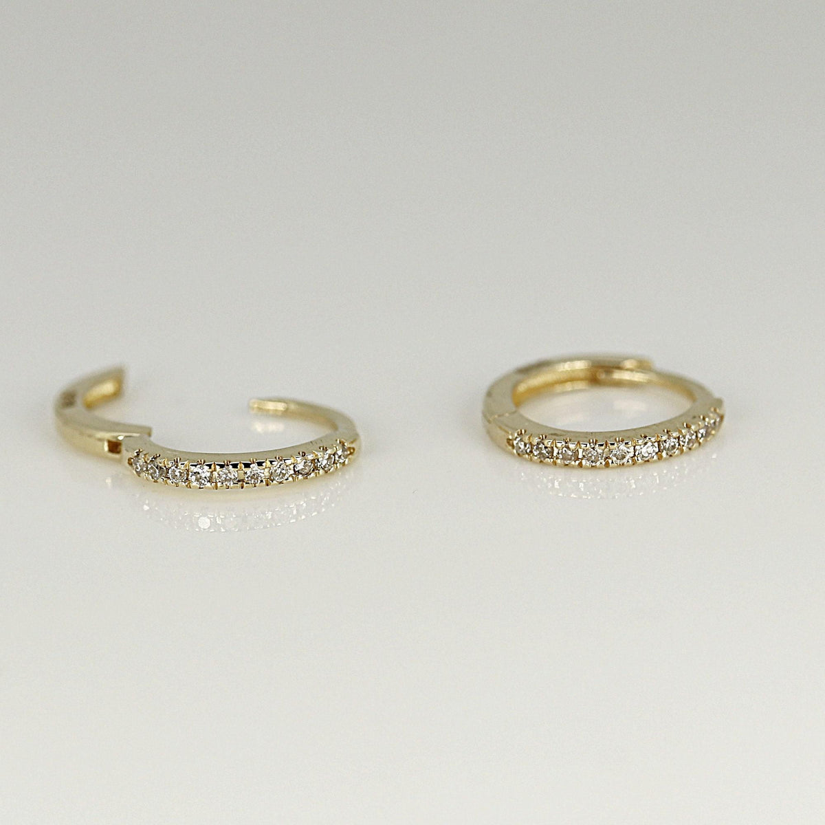 Two small gold hoop earrings studded with tiny diamonds lying on a flat white surface.