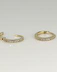 Two small gold hoop earrings studded with tiny diamonds lying on a flat white surface.