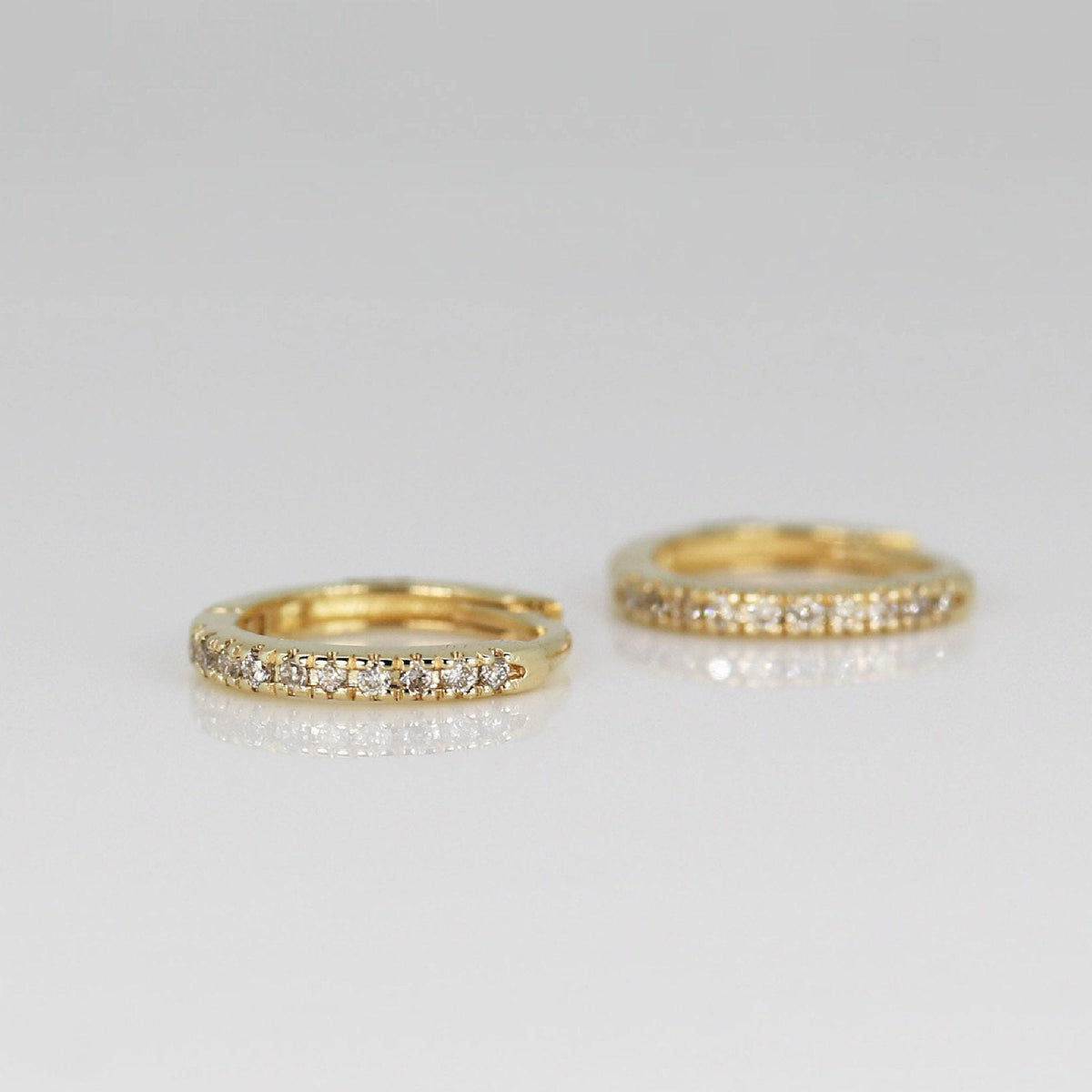 Two small gold pave diamond hoop earrings shown close up on a light surface.