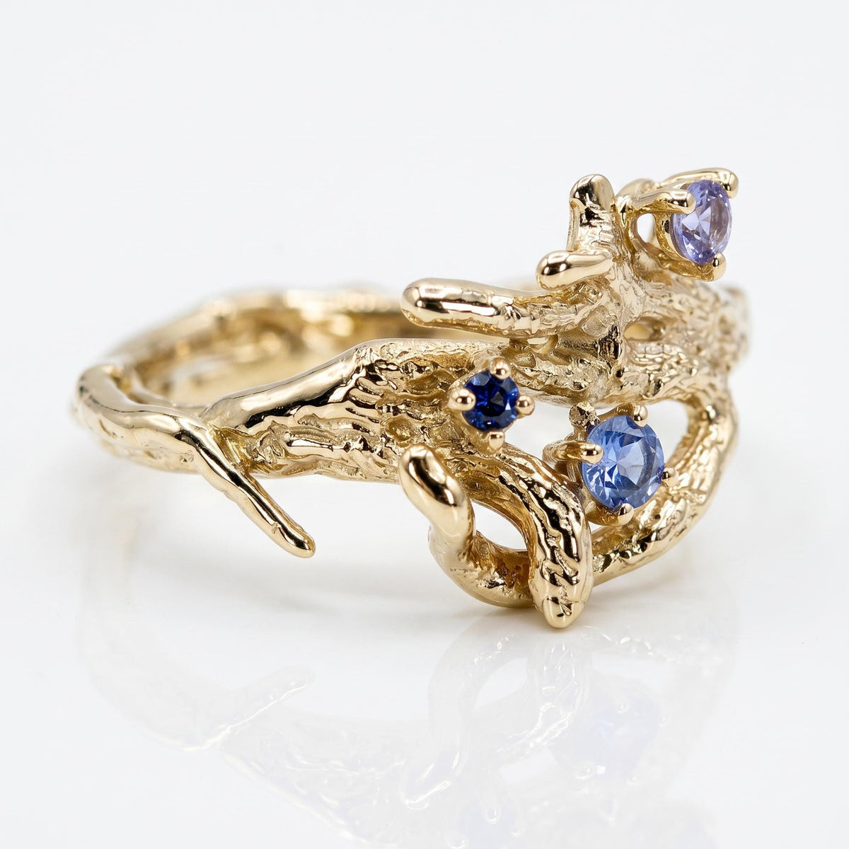 Side view of the gold twig ring showing its textured band and three flush-set blue and lilac sapphires against a white background.