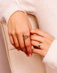 A person wearing two gold rings on their hands, including the textured branch ring and a ring with a marquise stone, against a cream sweater.