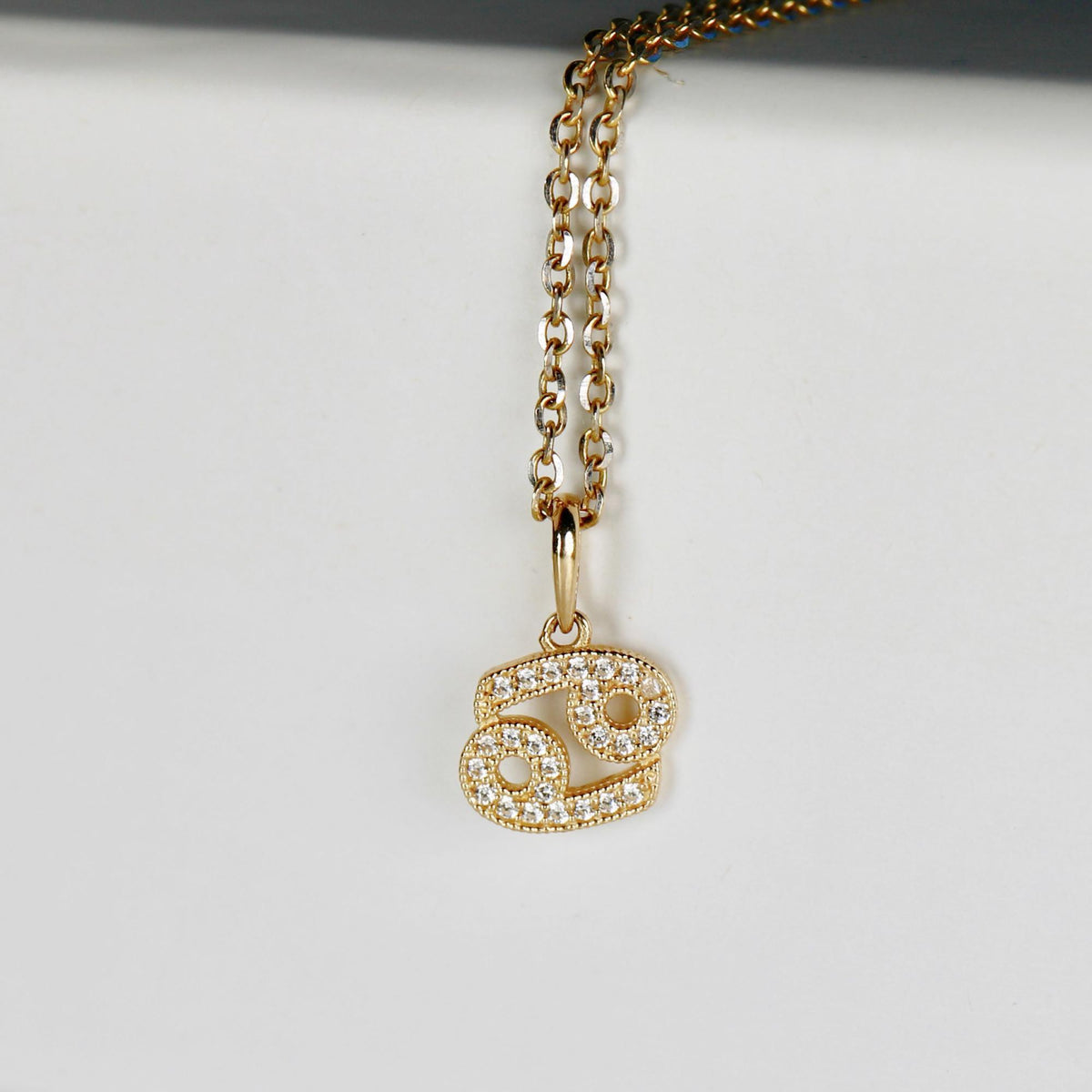 A close-up view of a gold chain necklace featuring a Cancer zodiac sign pendant paved with small round diamonds.
