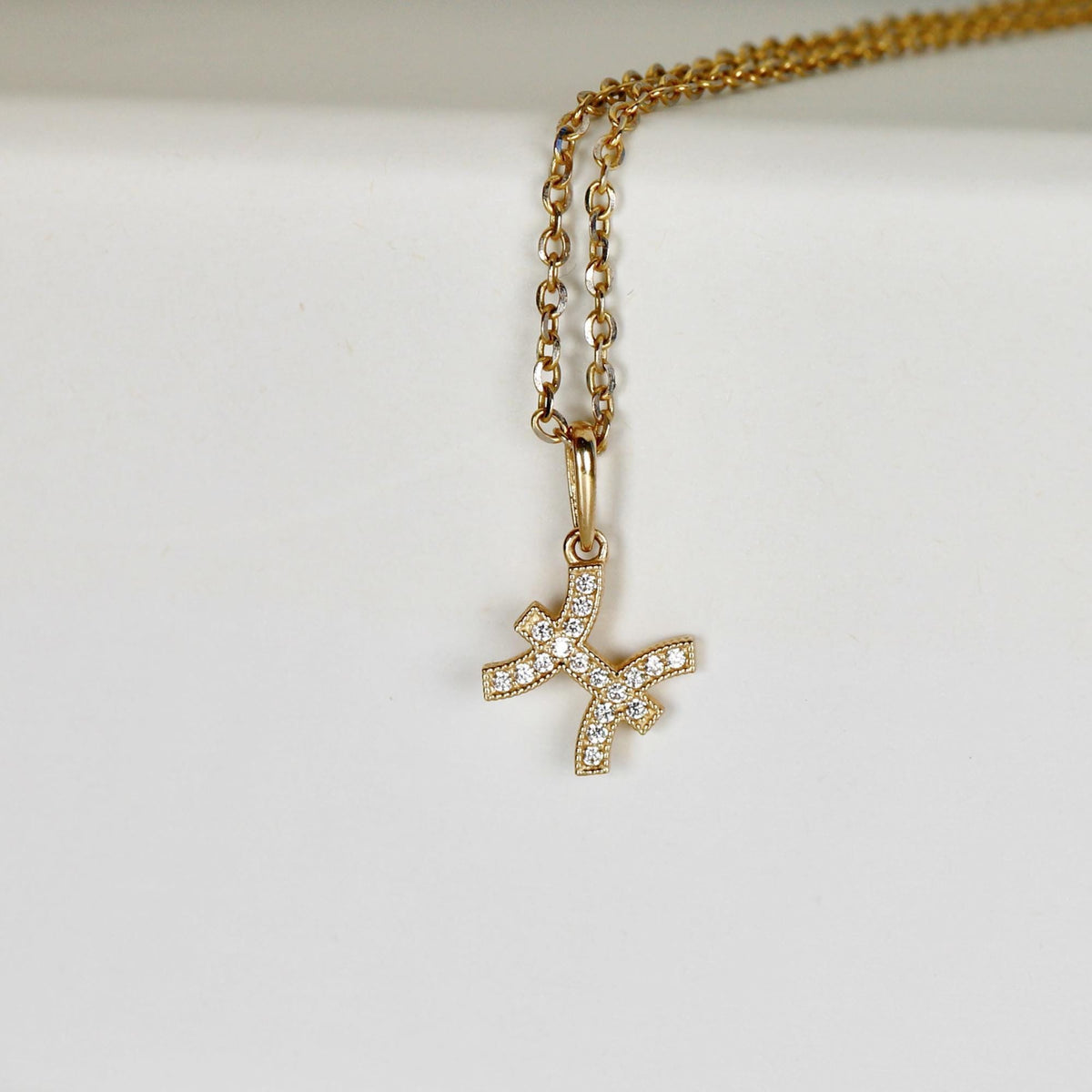 A gold chain necklace rests on a white surface, showcasing a Pisces zodiac pendant encrusted with small diamonds.