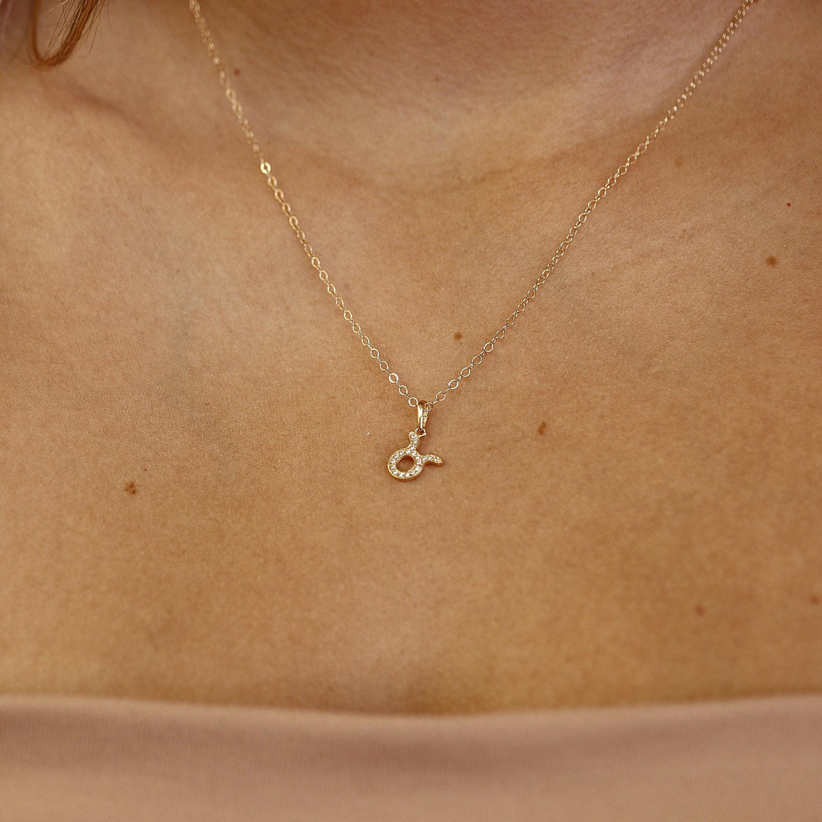 A close-up shot of a gold link chain necklace with a sparkling Taurus pendant resting on a person&amp;