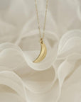 A gold crescent moon pendant necklace displayed on soft, draped white fabric.