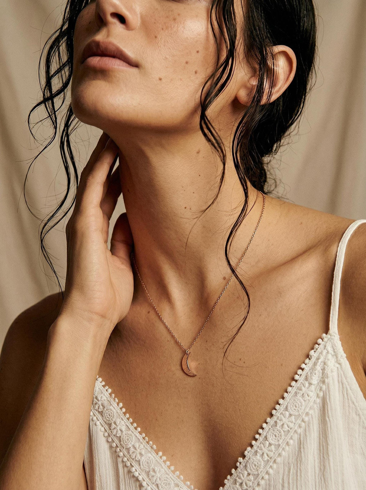 A close-up of a person wearing a gold crescent moon pendant necklace with their hand near their neck.