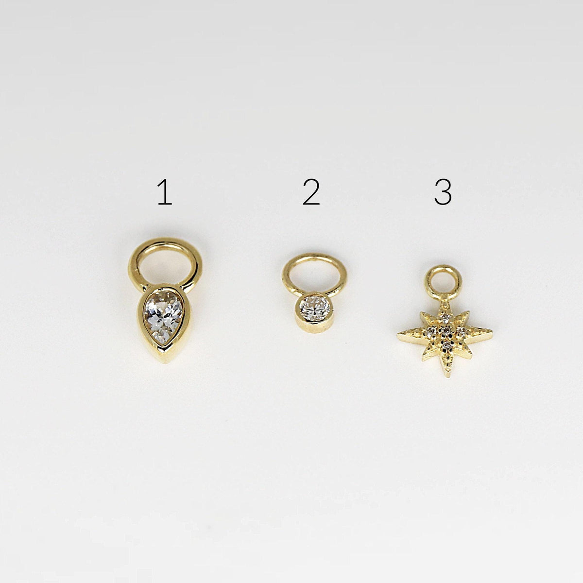 Three gold charms labeled 1 through 3, featuring a pear-shaped stone, a round bezel-set stone, and a pavé-set starburst charm on a white background.