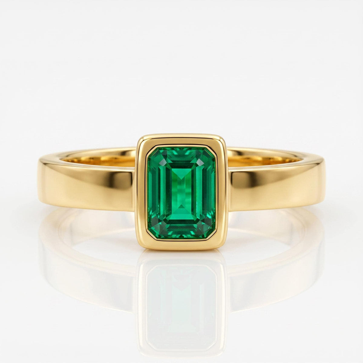 Front view of a gold ring featuring a bezel-set emerald-cut green gemstone on a reflective white surface.