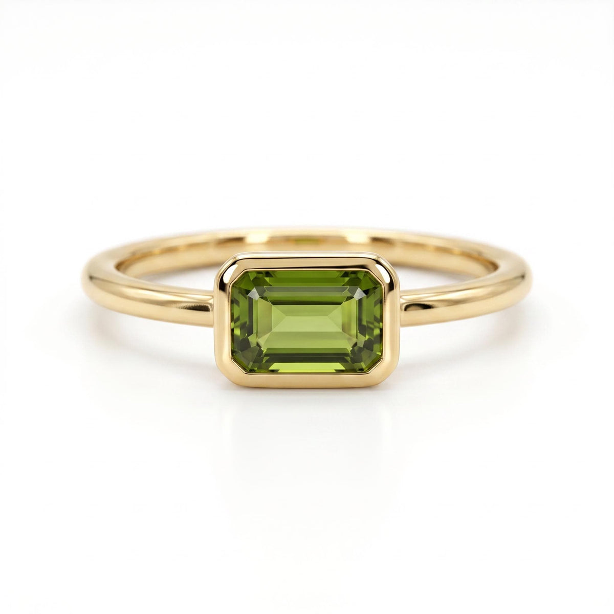A gold ring with a bezel-set horizontal emerald-cut green gemstone against a white background.