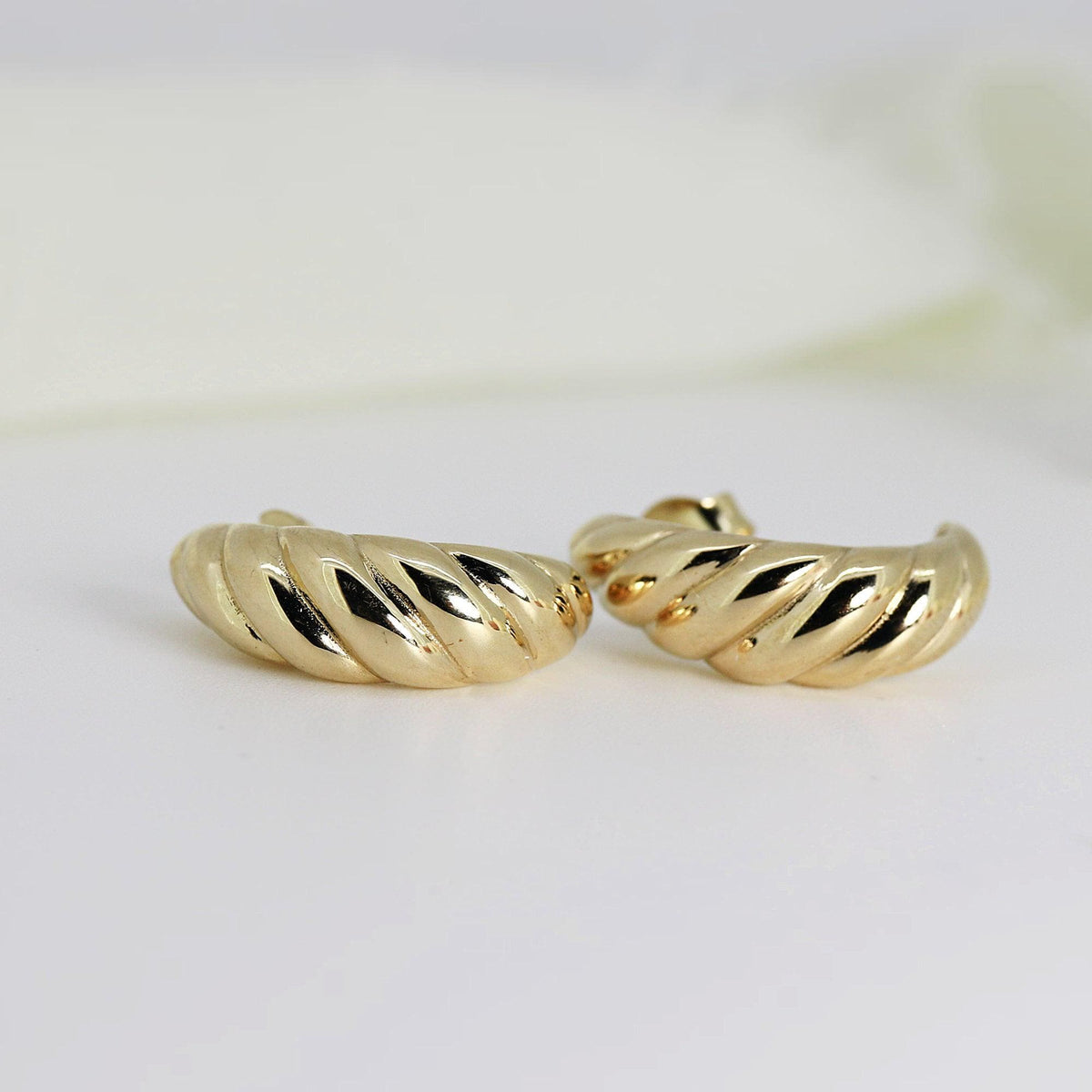 Two thick, polished gold croissant hoop earrings lie flat on a white surface.