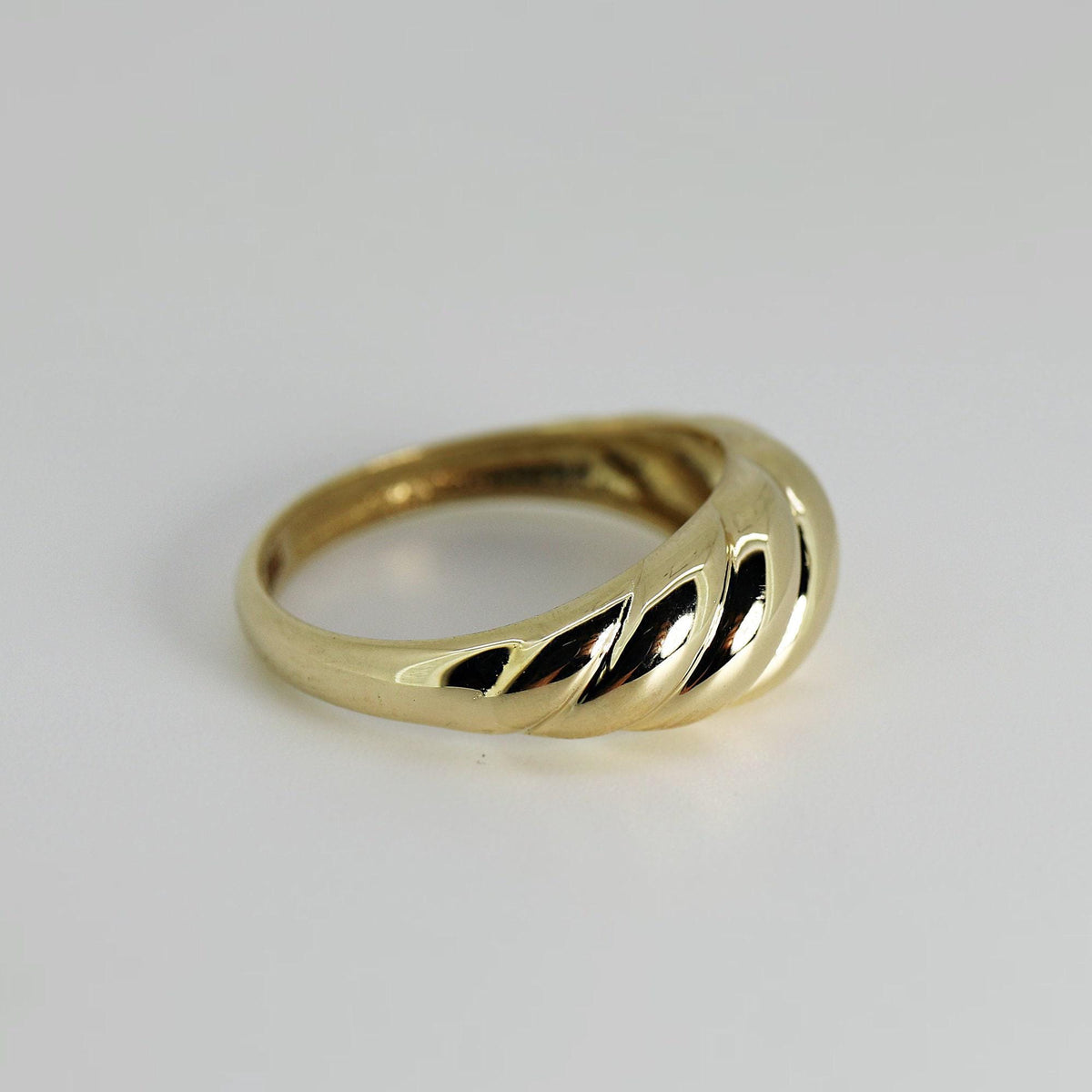 An angled view of a gold ribbed ring on a white surface.