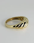 An angled view of a gold ribbed ring on a white surface.