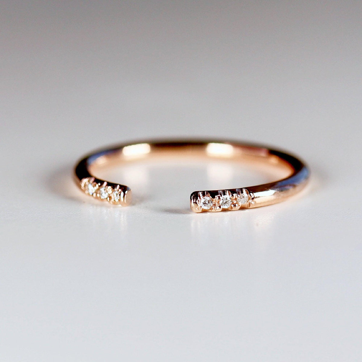 A close-up view of an open rose gold cuff ring with small pave diamonds on the ends.