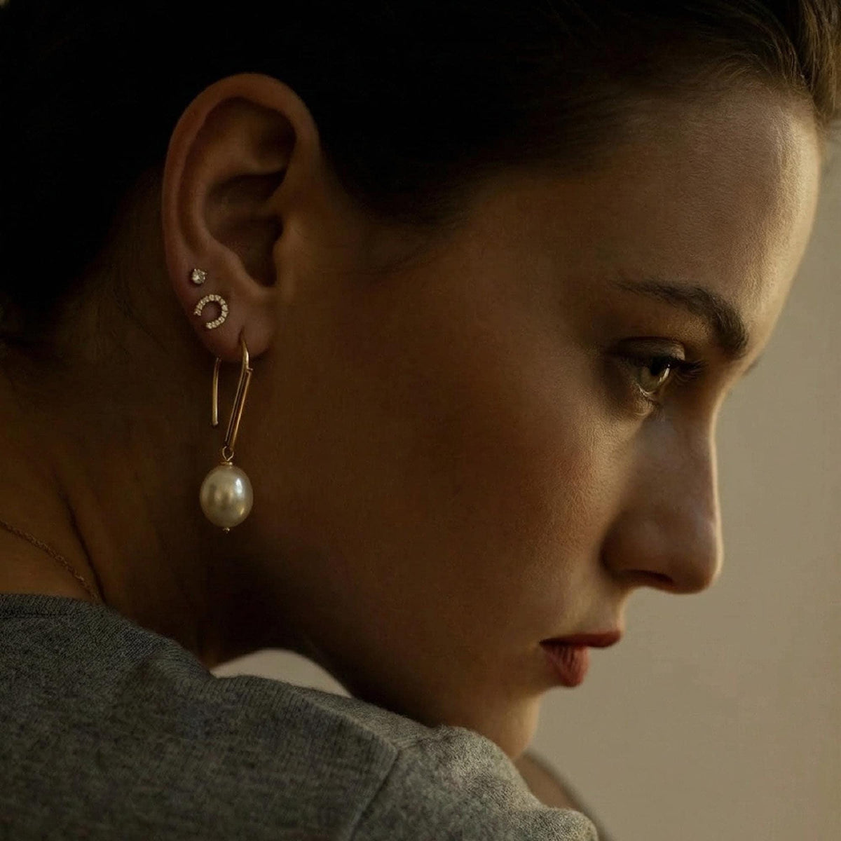 A close-up profile of a woman wearing one of the gold and pearl dangle earrings in her earlobe, with two smaller stud earrings in her upper ear.