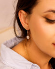 Profile shot of a woman wearing the gold pearl dangle earring and multiple small stud earrings, dressed in a light blue button-down shirt.