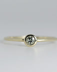 Front-facing, close-up view of a thin gold ring with a round, bezel-set light green gemstone.