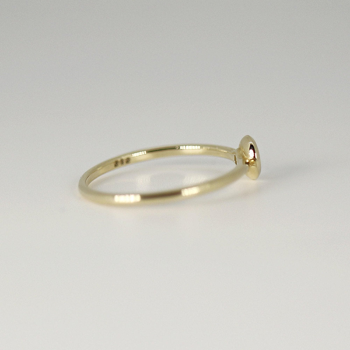 Profile view of a thin gold band resting on a white surface, showing the side profile of the bezel setting.