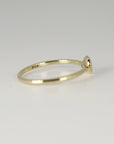 Profile view of a thin gold band resting on a white surface, showing the side profile of the bezel setting.