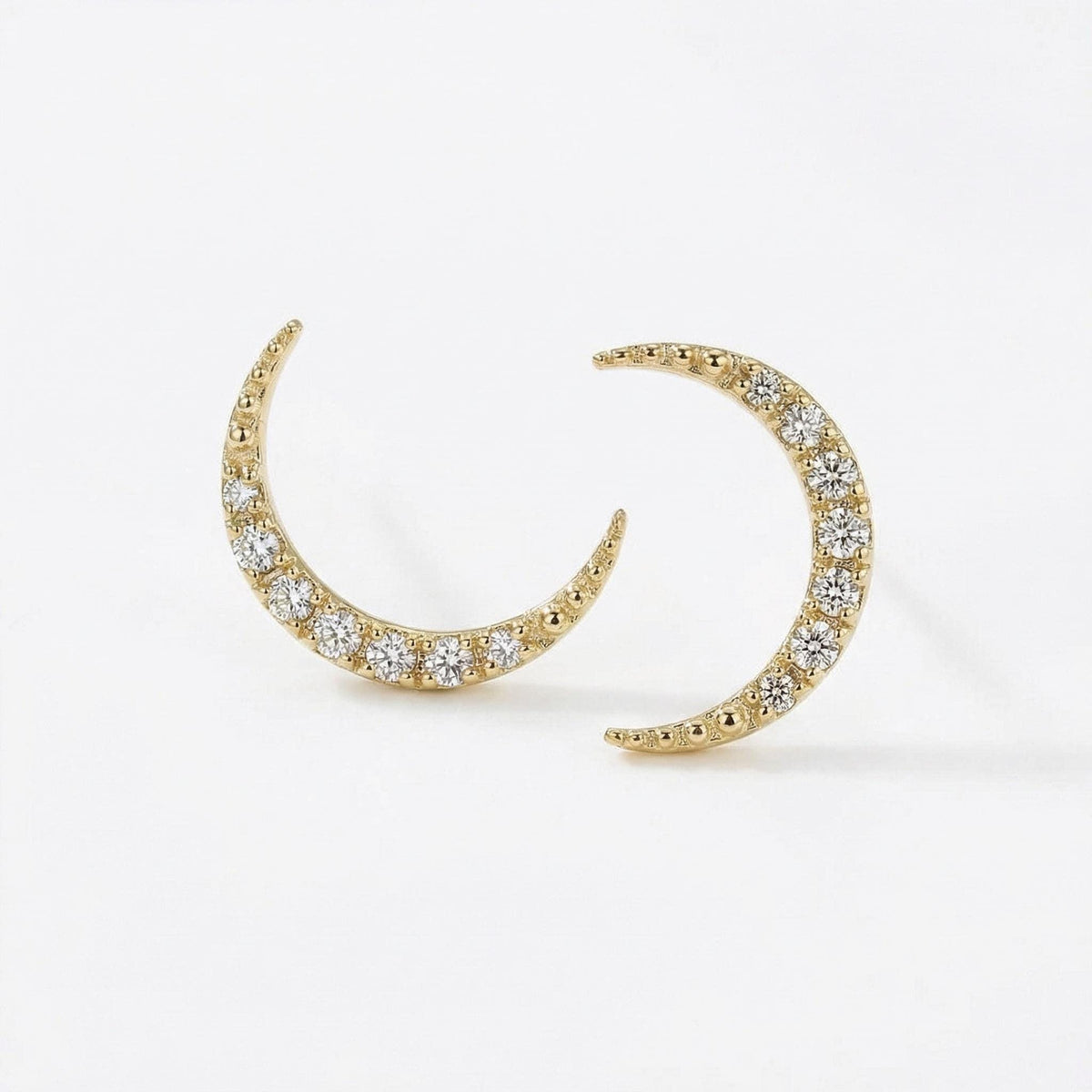 Two gold crescent moon stud earrings set with round diamonds are displayed at a slight angle on a white surface.