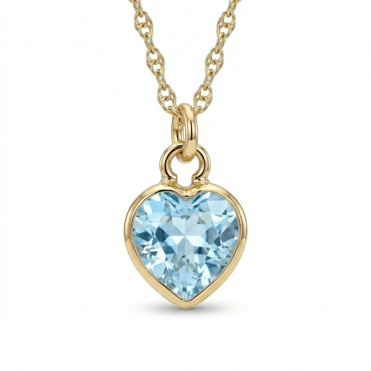A gold chain necklace holds a faceted heart-shaped light blue gemstone pendant against a white background.