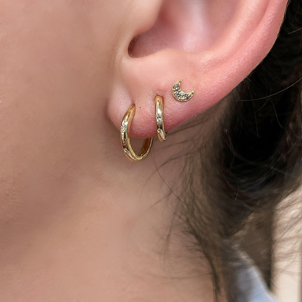 Close-up of an earlobe wearing two gold hoop earrings and a small star stud on the cartilage.