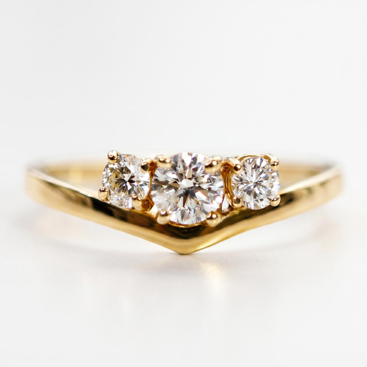 Close-up shot of the gold V-shaped ring showcasing the graduated three-stone diamond setting.