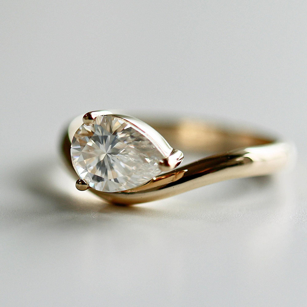 A detailed product shot of the gold pear moissanite ring on a plain surface.