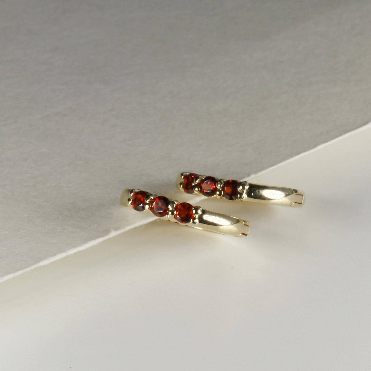 Two gold trio stone hoop earrings displayed on a white and light gray angled surface.